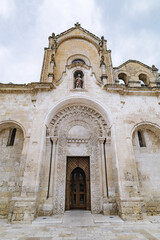 Matera, Italy. Facade of ancient Church of San Giovanni Battista in Matera’s historic center. Romanesque architecture with intricate stone carvings and religious statue above the portal. 