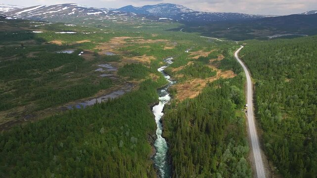 Drone view of Gaustafallet waterfall flowing through vegetations next to the E14 highway at sunset