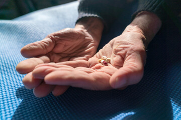 Grandfather's hands with several pills resting on a blue carpet, illuminated by warm natural sunlight.