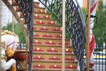 Close-up view of a colorful staircase on a vintage carousel, featuring decorative lights, ornate...
