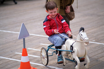 A boy plays with a ride on toy horse, smiling as he steers the wheeled toy. Childhood fun and play concept. A child aged 3 years