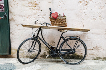 Matera, Italy. An old bicycle leans against a stone wall in Sassi di Matera, Italy, with a basket holding wine bottle and a red heart, used as a charming display or rustic street decor. 