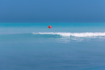 Bright red buoy as boundary of swimming area on turquoise calm sea water on sunny day