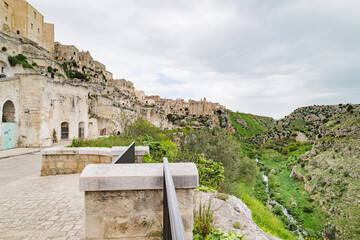 Matera, Italy. View of Via Madonna delle Virtù in the Sassi di Matera, Italy. In the distance, the Convento di Sant’Agostino crowns the hilltop. Below right flows the Gravina torrent.