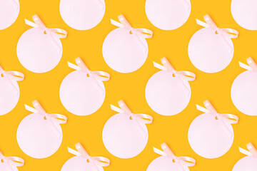 Repetitive pattern made of pink round empty tag with tied ribbon bow on a yellow background.