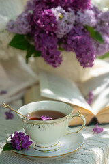 A bouquet of lilacs on the table and a cup of tea.