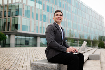 Professional man working on laptop outdoors in a modern urban setting, showcasing determination and...