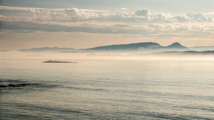Fototapeta premium Misty morning over calm ocean with distant mountains in background 