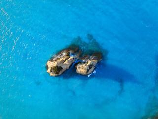 Rocks in the middle of the sea. Clear blue water and waves. Marine natural landscape. Summer seascape. Aerial view. Image for cards, background, wallpaper or design.