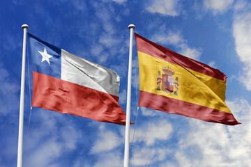 Chile and Spain flags waving under a bright sky, symbolizing unity, heritage, and cultural ties. The red, white, star of Chile meets Spain's red, yellow, and coat of arms, representing strength.