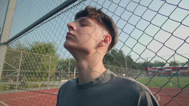 Teenage Guy Chillin by Sports Field Fence, Basking in Afternoon Sun