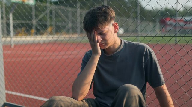 Teen sits in silent stress near fenced school sports area