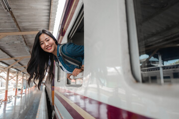 Happy asian tourist leaning out of train window smiling at railway station