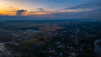 A breathtaking aerial panoramic view of a vibrant sunset illuminating the sky above a lush green hilltop with a small structure, surrounded by scattered clouds and distant landscapes.