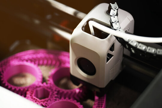 3D printing of a magenta planetary gear model &ndash; macro close-up of FDM printer extruder depositing filament for mechanical engineering rapid prototyping and additive manufacturing.