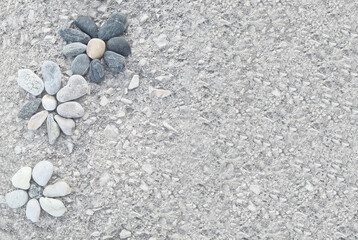 Three stylized flower designs are arranged on a light gray gravel ground.  The flowers are composed of various sized and colored stones, including shades of gray, black, beige, and white. 