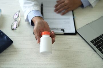 Doctor with stethoscope who is sitting in hospital clinic is holding an medicine bottle to assess the quality of medicine, recommending medication to patient and explaining the dose and description.