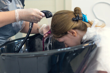 little girls wash their strands after coloring in a beauty salon.
