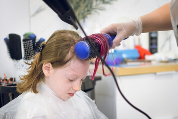 A little girl's hair is dried with a hair dryer after coloring in a beauty salon.