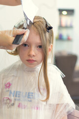 A little girl has her hair dyed bright pink in a beauty salon.