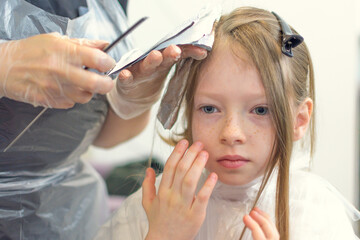 A little girl has her hair dyed bright pink in a beauty salon.