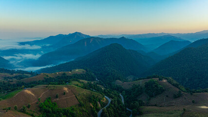 A breathtaking aerial view of a mist-covered forest at sunrise. The dramatic cloudscape and soft...