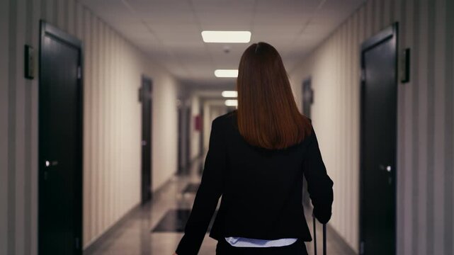 Red-haired businesswoman with suitcase looking at hotel room number on keycard