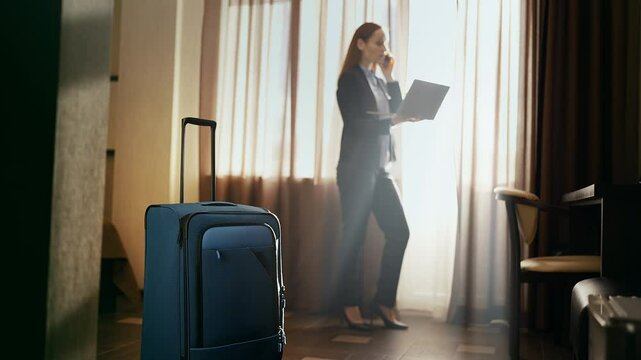 Female CEO talking on phone and working on laptop in hotel room, business trip