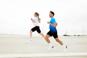 Morning joggers sprinting up white stairs in a vibrant urban park against a cloudy sky during early...