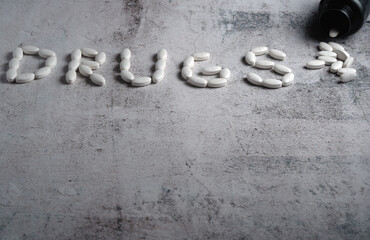 White oval pills spill from an overturned bottle next to the word 