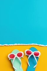 Minimal summer background with flip flops and sunglasses on a half yellow and blue paper.