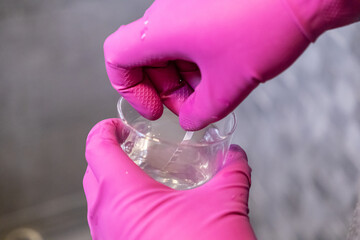 Hands in vibrant pink gloves precisely dipping a water test strip into a clear cup, assessing...