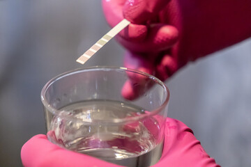 Person in pink gloves testing water quality with a reagent strip and glass of water, highlighting...