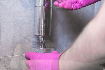 Hand in pink glove collecting pure water from a chrome shower filter, demonstrating domestic...