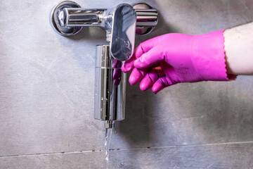 Hand in pink glove adjusts modern chrome shower water filter, ensuring purified liquid flow for...