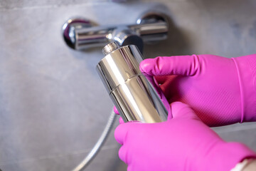 Person in vibrant pink gloves diligently installing a new chrome water filter onto a modern shower,...