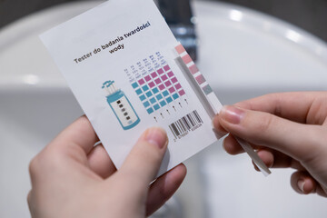Hands holding a water hardness test strip with instructions (Water hardness test), assessing water quality for effective home filtration systems © Alina