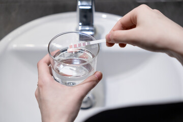 Hands testing tap water quality with a chemical strip in a glass, ensuring purity and safety for household use