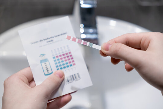 Hands holding a water hardness test strip with comparison chart, evaluating home water quality for shower filter effectiveness and personal health management