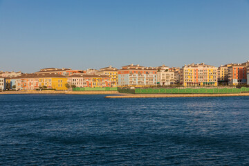 Fototapeta premium Doha, Qatar - 13 June 2025: A scenic view of vibrant residential buildings along the coast of The Pearl Island in Doha, Qatar the image shows colorful architecture, calm sea water
