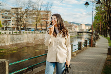 Young caucasian woman walk home from work drink coffee and use smartphone	
