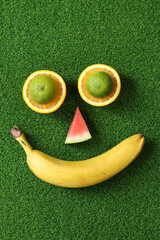 Fruity smiling abstract face. Banana, watermelon slice, oranges and limes on green grass...