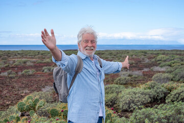 Happy senior man with backpack in a trekking day in country footpath along the sea, enjoying...
