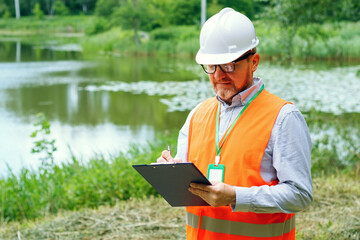 Fototapeta premium Male forestry inspector studying the condition of trees near water in the forest. Ecologist's work. Conducting environmental monitoring.