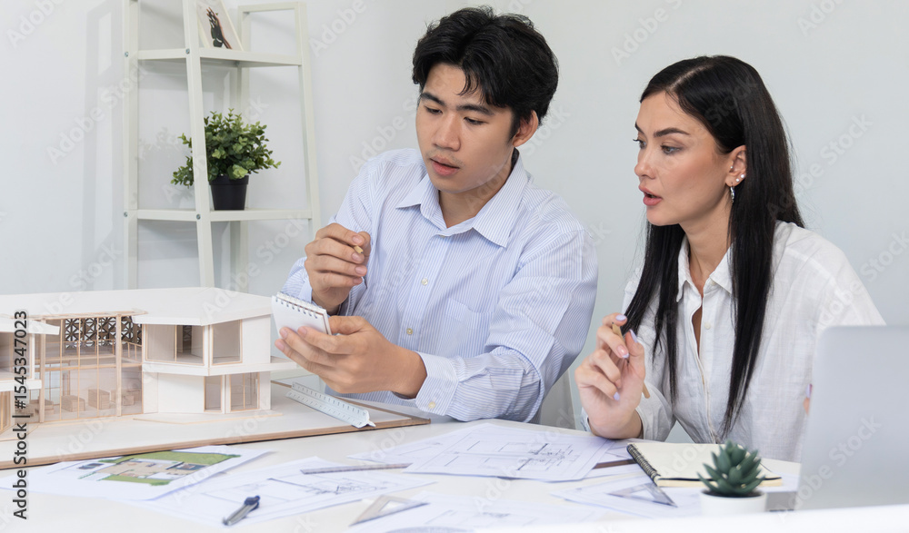 Poster professional male asian architect using ruler to measure house model length while young beautiful ca