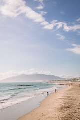 A scenic view of a sunlit beach with gentle waves lapping against the shore and people enjoying a...