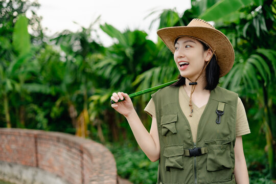 Young Asian woman enjoying nature in a tropical garden while wearing a straw hat and a vest during daytime exploration