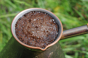 Coffee in a copper pot on a background of green grass