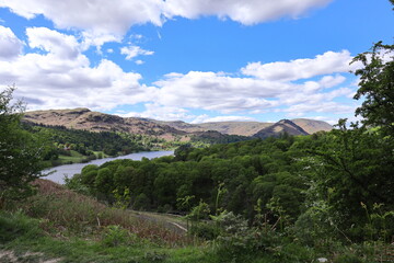 Panoramic view from a hillside above Grasmere, overlooking a dense green forest, calm lake and...