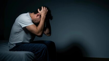 A man sitting on a bed distressed, holding his head, conveying mental health struggles, nightmares, and sleep issues footage.
